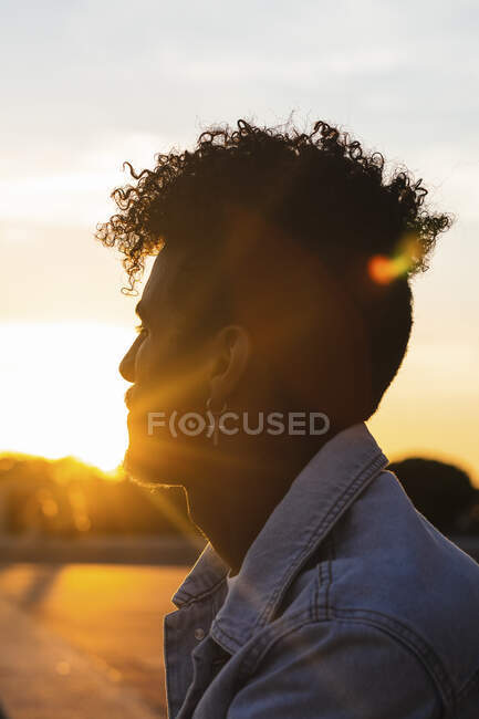 Primo piano del giovane che indossa orecchino a forma di croce contro il cielo durante il tramonto — Foto stock