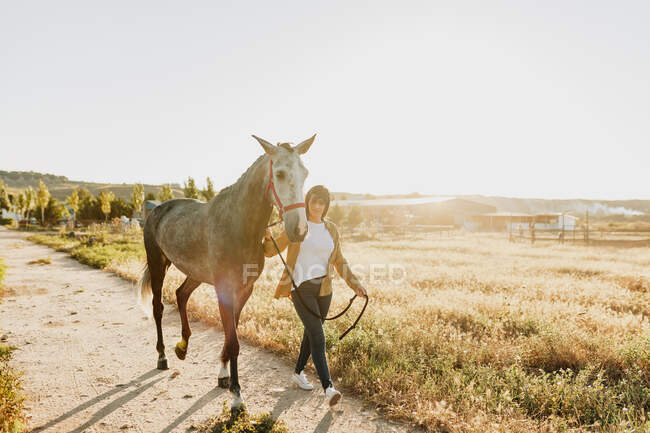 Donna che cammina con cavallo sul sentiero durante la giornata di sole — Foto stock