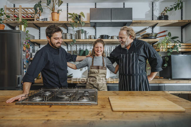 Chefs felices de pie con el brazo alrededor del otro en la cocina - foto de stock