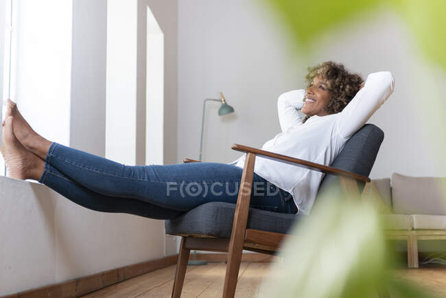 Духовна жінка з руками позаду голови розслаблює крісло вдома. — стокове фото