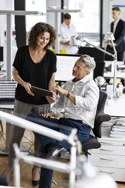Бизнесмен и женщина работают над цифровым планшетом с коллегами на заднем плане в офисе открытого плана — стоковое фото