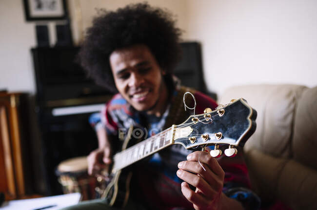 Jeune guitariste masculin ajustant les cordes de l'instrument à la maison — Photo de stock