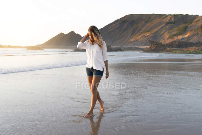 Mitte erwachsene Frau schaut beim Spazierengehen im Wasser am Strand nach unten — Stockfoto