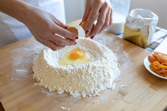 Femme casser oeuf dans la farine sur planche à découper dans la cuisine — Photo de stock