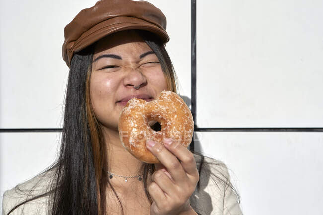 Junge Frau zwinkert bei sonnigem Tag beim Donut-Essen — Stockfoto