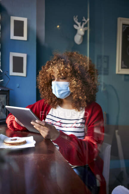 Frau trägt Hygienemaske mit digitalem Tablet im Sitzen — Stockfoto