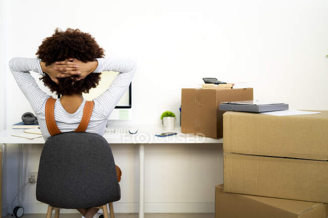 Afro donna con mano dietro la testa rilassante da scatole di cartone in nuova casa — Foto stock