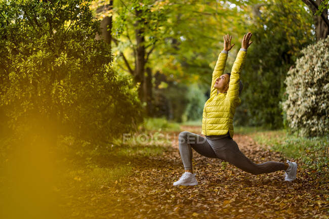 Atleta con la mano levantada haciendo yoga mientras hace ejercicio en el sendero en el parque - foto de stock