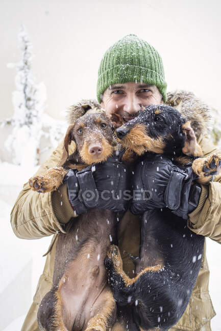 Homem maduro abraçando cães enquanto levanta durante o inverno — Fotografia de Stock