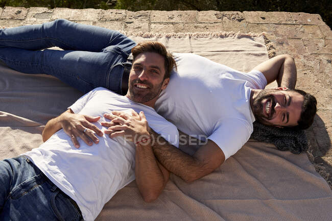 Sonriente pareja gay cogido de la mano mientras está acostado en manta - foto de stock