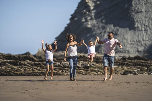 Ragazza guardando i genitori oscillare fratello mentre si cammina in spiaggia — Foto stock