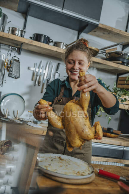 Jeune chef souriant tout en marinant de la viande de poulet debout dans la cuisine — Photo de stock