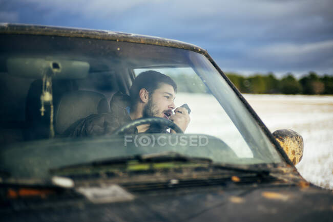 Jeune homme en voiture utilisant CB Radio en regardant par la fenêtre pendant le voyage — Photo de stock