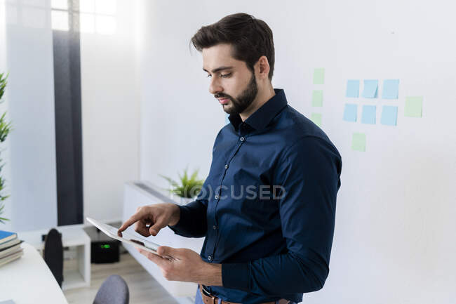 Чоловічий підприємець використовує цифрову табличку проти стіни в офісі — стокове фото