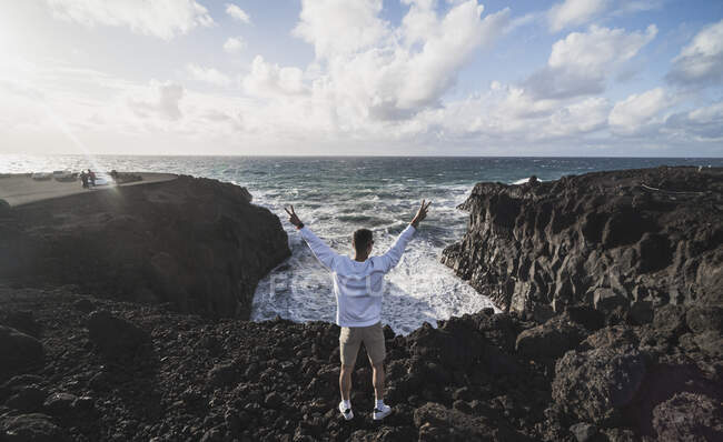 Un touriste masculin signe de paix debout sur une roche volcanique pendant une journée ensoleillée à Los Hervideros, Lanzarote, Espagne — Photo de stock