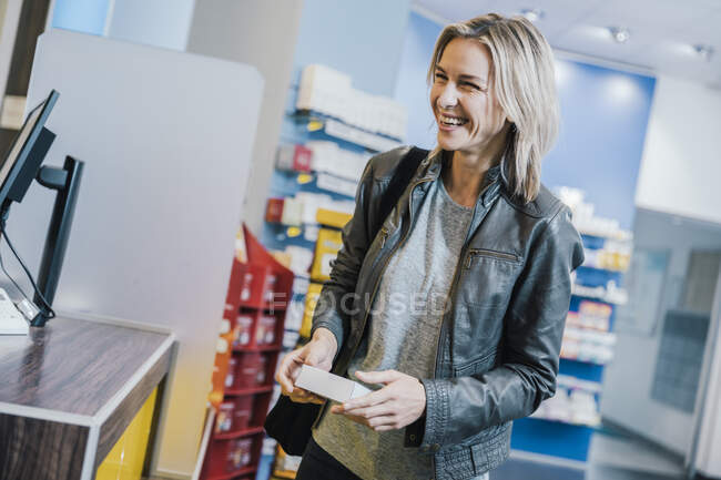 Cliente sorridente con medicina in piedi al banco cassa in farmacia — Foto stock