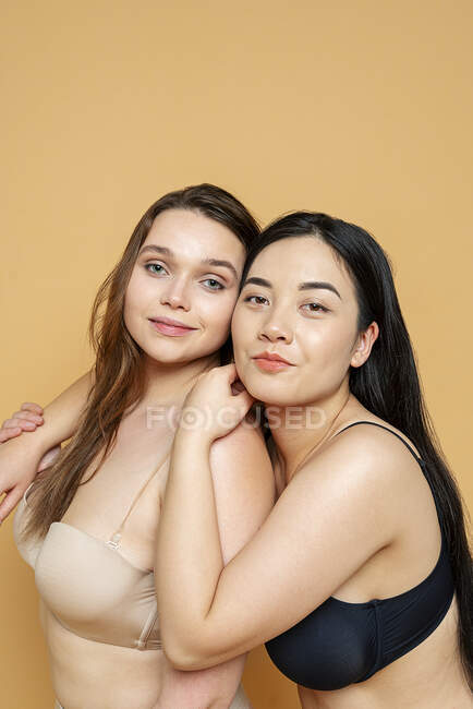 Lächelnde multiethnische Models in Dessous umarmen sich, während sie vor gelbem Hintergrund stehen — Stockfoto