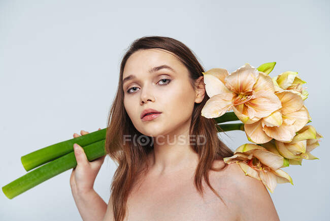 Donna senza maglietta con mazzo di fiori che fissano mentre in piedi in studio — Foto stock