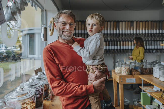 Зрелый отец носит сына, стоя в магазине розничной еды — стоковое фото