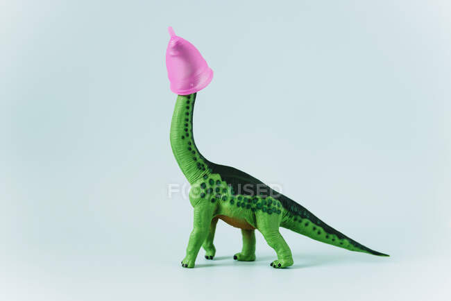 Diplodocus dinosaur toy with pink menstrual cup on the head on mint green background — Stock Photo