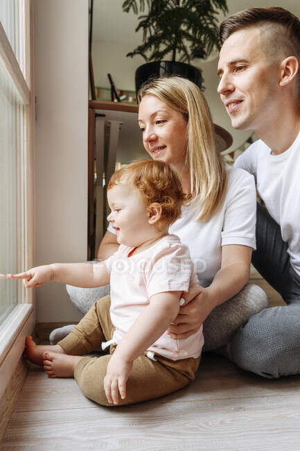 Famiglia felice con bambina che guarda attraverso la finestra — Foto stock