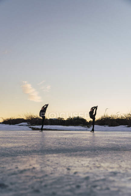 Deux patineuses pratiquant ensemble sur un lac gelé au crépuscule — Photo de stock