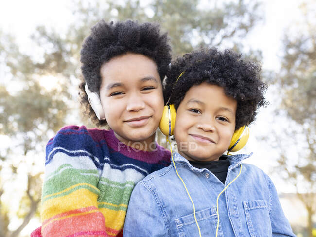 Fratello e sorella con le cuffie sorridenti seduti insieme al parco — Foto stock