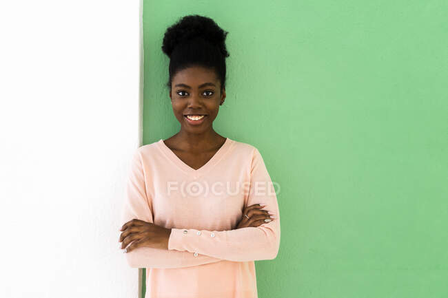 Smiling woman standing with arms crossed against multi colored wall — Stock Photo