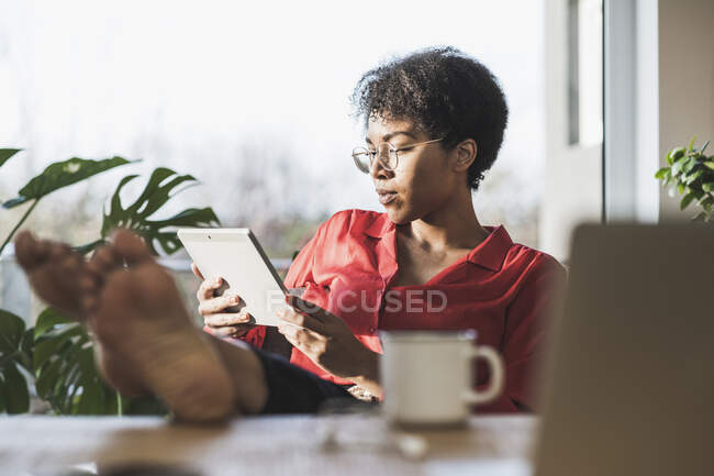 Жінка з голими ногами на столі за допомогою цифрового планшета. — стокове фото