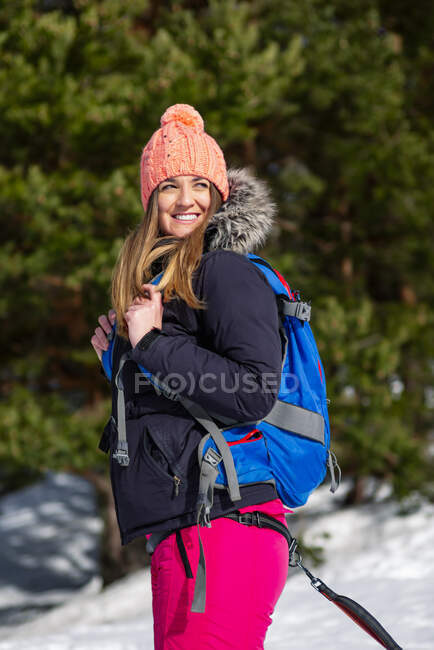 Donna sorridente con lo zaino distogliere lo sguardo durante l'inverno — Foto stock