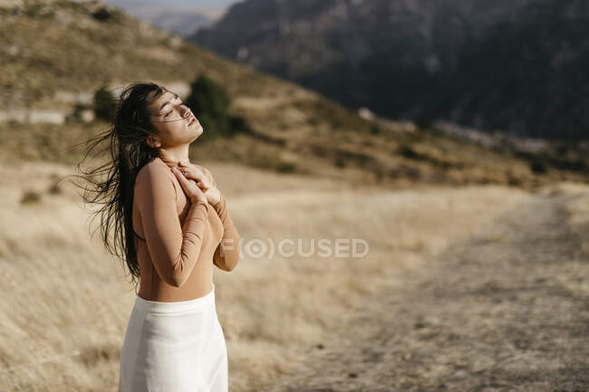 Jeune femme avec les yeux fermés debout dans le champ pendant le coucher du soleil — Photo de stock