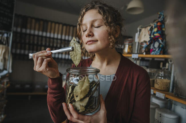 Female clerk with eyes closed smelling bay leaf while working in zero waste shop — Stock Photo