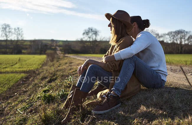 Coppia eterosessuale seduta sul campo durante il tramonto — Foto stock