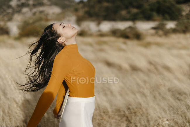 Беззаботная молодая женщина с закрытыми глазами, стоящая в поле в ветреный день — стоковое фото