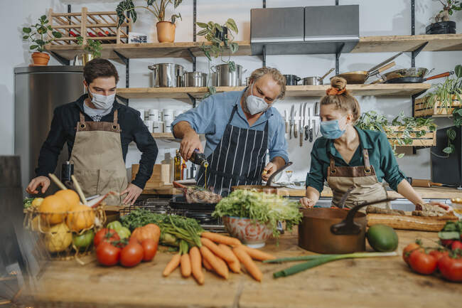 Equipo de cocineros con mascarilla protectora cocinando mientras trabajan juntos en la cocina - foto de stock