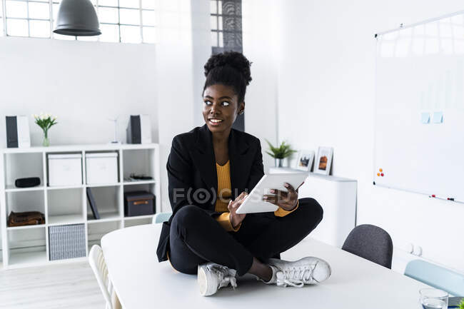 Думлива молода жінка професійний сидячи крос-ніг з цифровим планшетом на столі в офісі — стокове фото