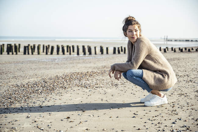 Belle femme avec position accroupie regardant loin de la plage par une journée ensoleillée — Photo de stock