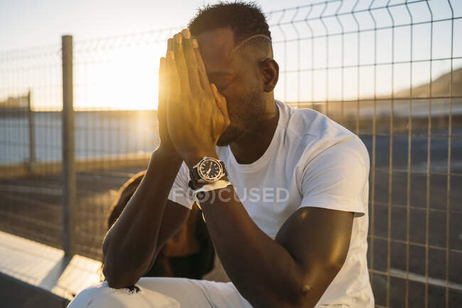 Thoughtful man with hands clasped sitting against fence — Stock Photo