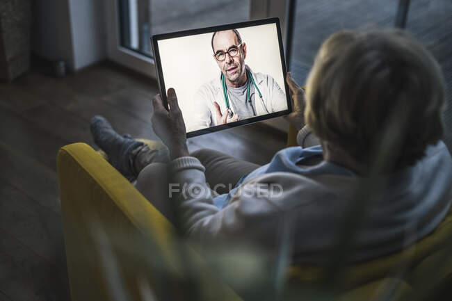 Senior woman on video call with male doctor through digital tablet in living room — Stock Photo