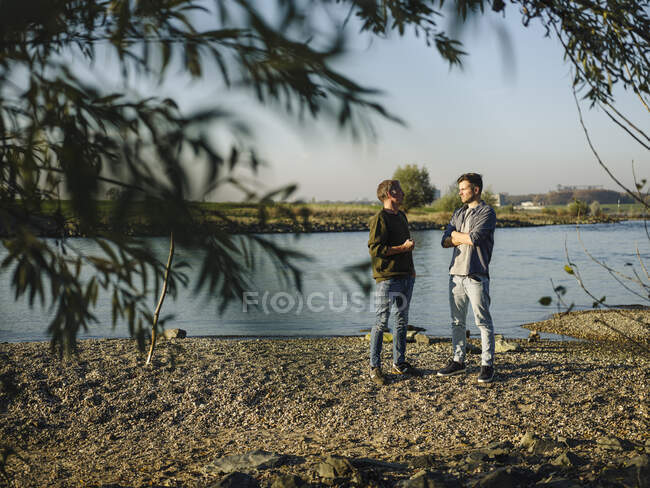 У сонячний день син і батько розмовляють один з одним на березі річки. — стокове фото