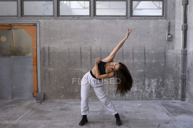 Жіноча танцівниця практикується проти стіни на покинутій фабриці. — стокове фото