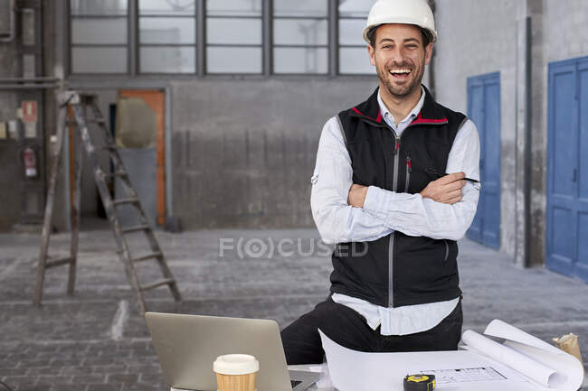 Male architect with arms crossed laughing while standing at table in building — Stock Photo