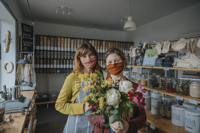 Female entrepreneur with clerk holding bunch of flowers while standing in retail store during pandemic — Stock Photo