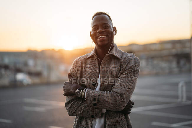 Homem alegre com os braços cruzados de pé no estacionamento durante o pôr do sol — Fotografia de Stock