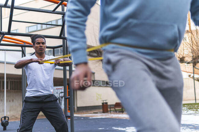 Giovane uomo tenuta stretching band durante l'esercizio con un amico in città — Foto stock