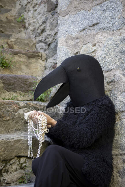 Woman in crow costume looking at jewelry by staircase — Stock Photo