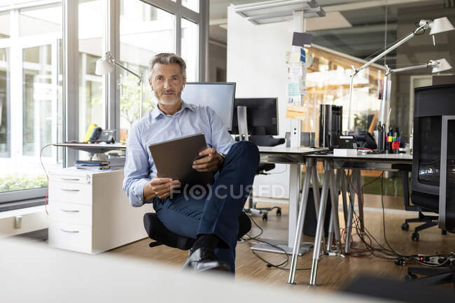 Confident entrepreneur with digital tablet sitting at open plan office — Stock Photo