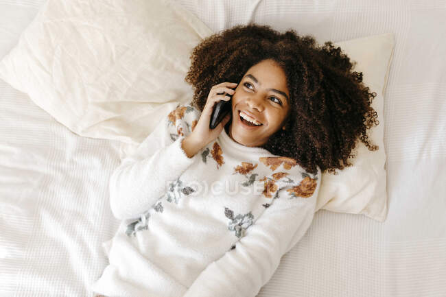 Mulher excitada falando no celular enquanto deitada na cama em casa — Fotografia de Stock