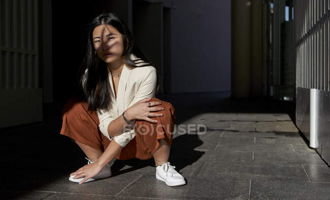 Jeune femme accroupi par la porte avec ombre à la main sur le visage — Photo de stock