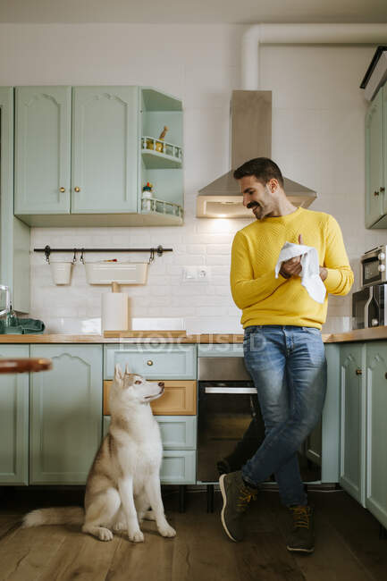 Mitte erwachsener Mann trocknet Hände, während er Siberian Husky Dog in der Küche ansieht — Stockfoto